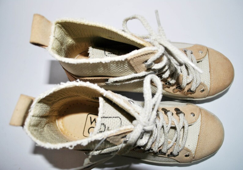 May include: A pair of beige canvas high-top sneakers with white laces and a brown leather trim. The sneakers have a woven texture and the brand name "WC" is visible on the inside of the shoe.