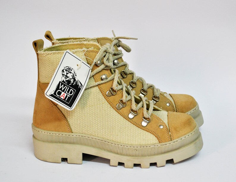 May include: Beige and brown hiking boots with a white rubber sole. The boots have a lace-up closure and a tag that says "Wild Cat".