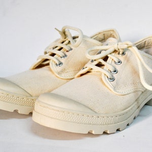 May include: A pair of off-white canvas low-top shoes with white laces. The shoes have a thick, white rubber sole.