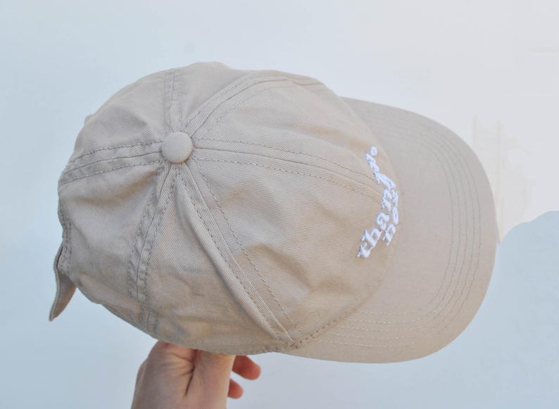 May include: A beige baseball cap with a white embroidered design that says "the days" on the side.
