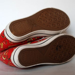 K&ouml;nnte beinhalten: Ein Paar rote Canvas-High-Top-Sneaker mit goldenem Muster. Die Schuhe haben wei&szlig;e Sohlen und braune Gummisohlen.