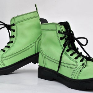Op de afbeelding: Een paar limoengroene combat boots met zwarte veters en zolen. De laarzen hebben een klassiek veterontwerp met zichtbare stikseldetails. De laarzen zijn gemaakt van een glad materiaal en staan tegen een witte achtergrond.