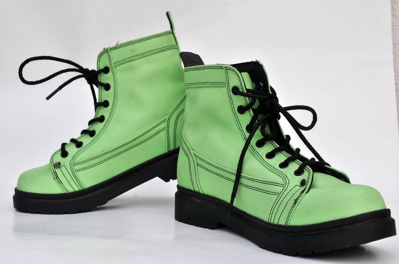 Op de afbeelding: Een paar limoengroene combat boots met zwarte veters en zolen. De laarzen hebben een klassiek veterontwerp met zichtbare stikseldetails. De laarzen zijn gemaakt van een glad materiaal en staan tegen een witte achtergrond.