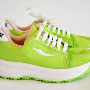 May include: A pair of bright green sneakers with white laces and a white sole. The sneakers have a white logo on the side and the word "ANA" on the back.