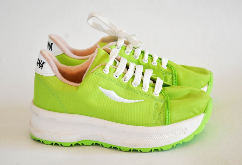 May include: A pair of bright green sneakers with white laces and a white sole. The sneakers have a white logo on the side and the word "ANA" on the back.