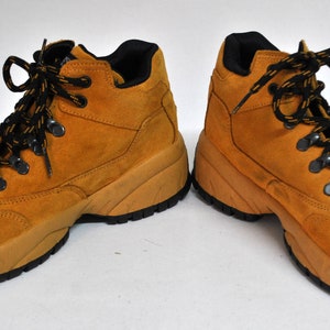 May include: A pair of tan suede hiking boots with black laces. The boots have a chunky sole and a lace-up closure.