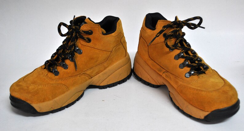 May include: A pair of tan suede hiking boots with black laces. The boots have a chunky sole and a lace-up closure.