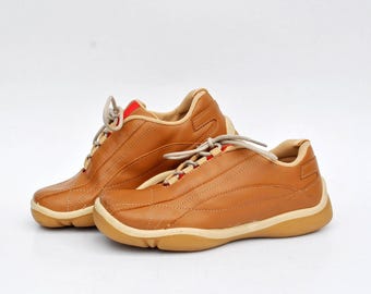 May include: A pair of brown leather sneakers with white soles and red laces. The shoes have a sporty design and are made of high-quality materials.