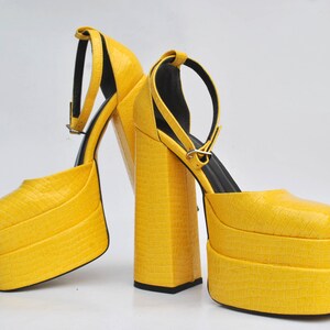May include: A pair of yellow platform heels with ankle straps. The heels are made of a textured material and have a chunky platform.