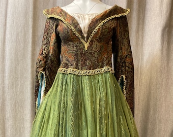 May include: A green and brown dress with a fitted bodice and a full skirt. The bodice has a floral pattern and is trimmed with gold lace. The skirt is made of a sheer fabric and has a layered look.