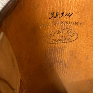 May include: Close-up of the inside of a brown leather shoe with the text "38314 MRS D KNIGHT" and a circular stamp that reads "DEHNERS OMAHA" in black ink.