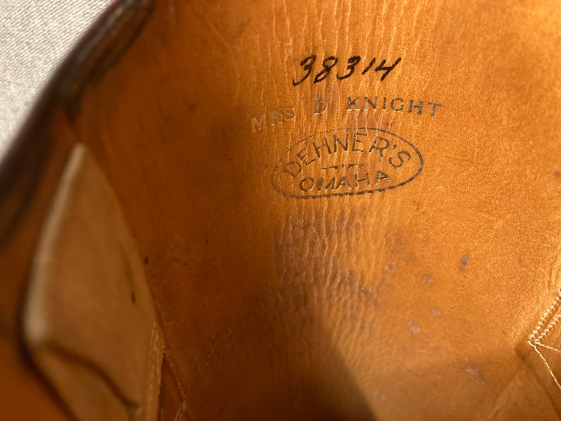 May include: Close-up of the inside of a brown leather shoe with the text "38314 MRS D KNIGHT" and a circular stamp that reads "DEHNERS OMAHA" in black ink.