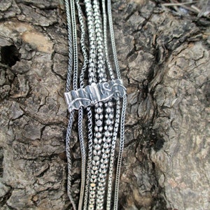 May include: A silver bracelet featuring multiple chains and a decorative clasp. The bracelet is crafted from various styles of silver chains, including a beaded chain, a rope chain, and a curb chain.
