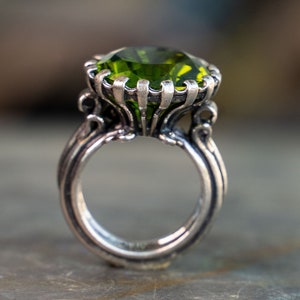 May include: A silver ring featuring a large, green gemstone set in an ornate, decorative setting.