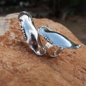May include: Two silver rings crafted from repurposed spoon handles. Each ring features a long, smooth, polished bowl section and a decorative handle end with a row of small, raised spherical beads along the side, reflecting light on the surface.