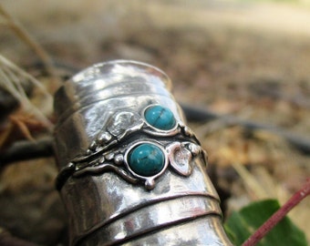 Puede incluir: Un anillo de banda ancha de plata con un acabado texturizado y martillado, que presenta dos cabujones de turquesa redondos y pulidos engastados en biseles de metal elevados. Incluye pequeñas esferas decorativas y detalles orgánicos.