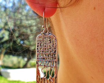 May include: A rectangular silver-toned metal earring featuring an intricate openwork design with a grid-like pattern at the top and vertical, flowing lines at the bottom, suspended from a simple curved hook wire.