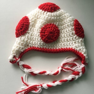 May include: White crocheted hat with red polka dots and a long white and red braided tassel.