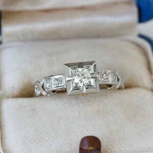 May include: A silver engagement ring with a square-cut diamond in a blue ring box.