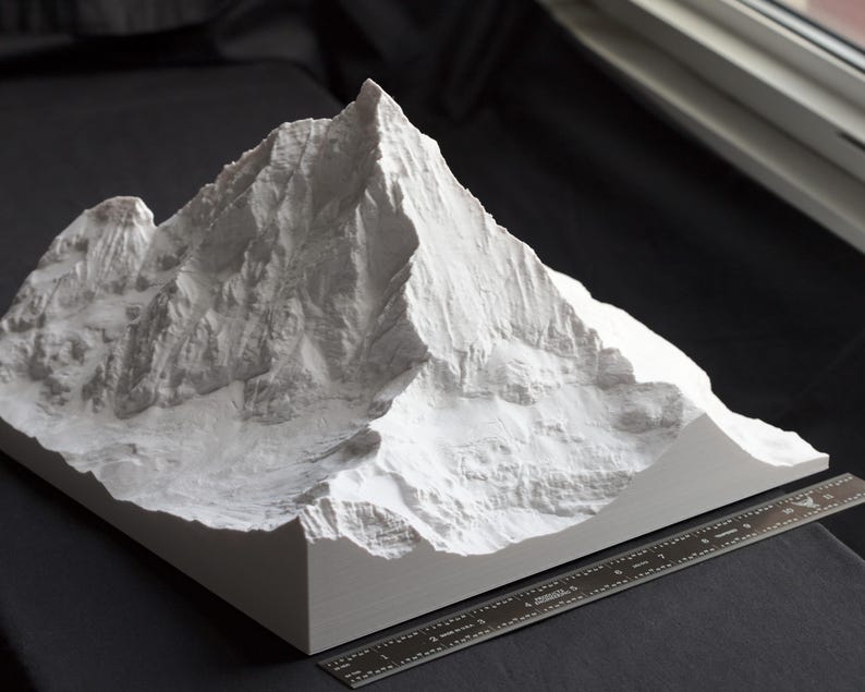 Puede incluir: Un modelo 3D impreso en blanco de una cordillera. El modelo es detallado y realista, con picos y valles agudos. El modelo est&aacute; sentado sobre una superficie negra.