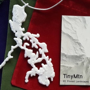 Può includere: Collana bianca stampata in 3D con una mappa dettagliata delle Filippine. La collana è esposta su una pochette in velluto rosso con un cartoncino bianco su cui è scritto "TinyMtn 3D Printed Landscapes".
