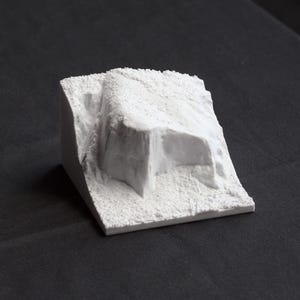 May include: A white, textured, 3D printed model of a rock formation. The model is designed to look like a small mountain or cliff.