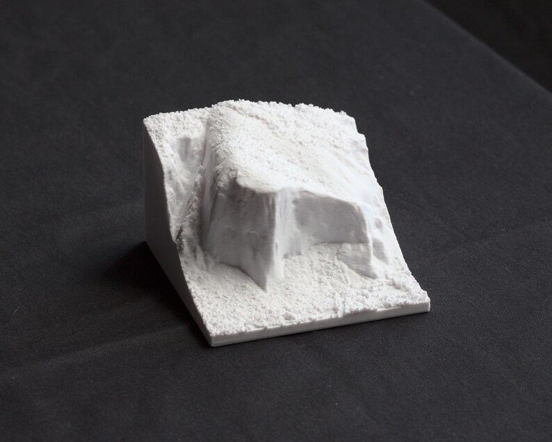 May include: A white, textured, 3D printed model of a rock formation. The model is designed to look like a small mountain or cliff.