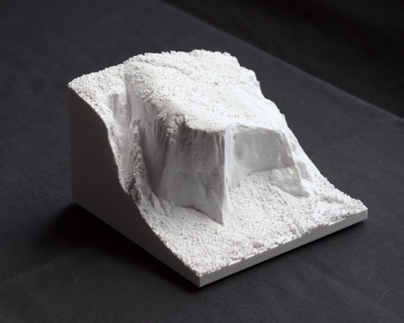 May include: A white plaster model of a mountain range with a textured surface.