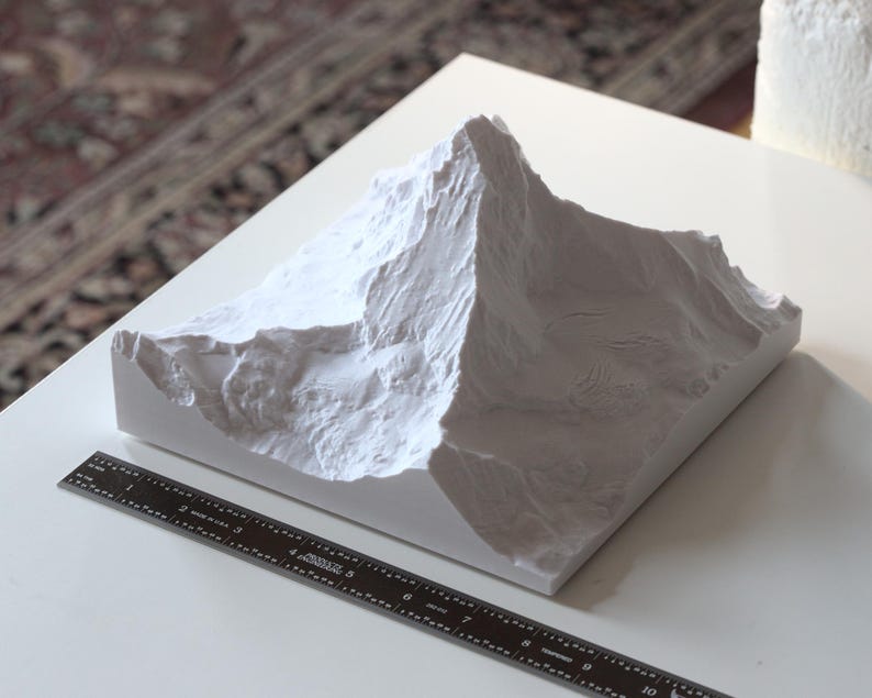 Puede incluir: Modelo de pico de monta&ntilde;a de yeso blanco, con una superficie texturizada, sobre una base blanca. El modelo mide aproximadamente 25 cm de ancho.