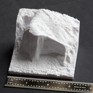 May include: White 3D printed model of a rocky cliff face. The model is textured to resemble a natural rock formation.