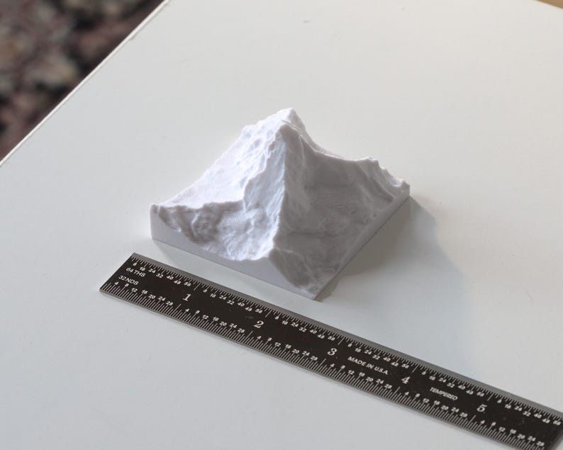 Puede incluir: Un modelo blanco de una cordillera de monta&ntilde;as impreso en 3D. El modelo mide aproximadamente 5 cm de alto y 7,5 cm de ancho. Una regla est&aacute; en primer plano para la escala.