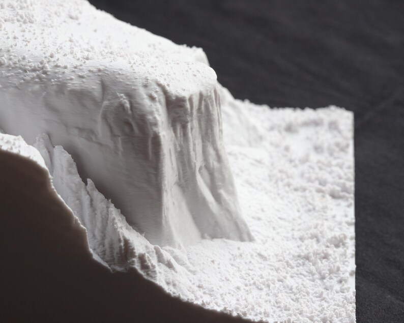 May include: A close-up of a white, textured, 3D printed model of a mountain range. The model is made of a smooth, white material and has a rough, textured surface.