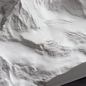 Puede incluir: Primer plano de un modelo de cordillera de monta&ntilde;as impreso en 3D blanco y texturizado. El modelo est&aacute; detallado con crestas y valles, creando una representaci&oacute;n realista de un paisaje monta&ntilde;oso.