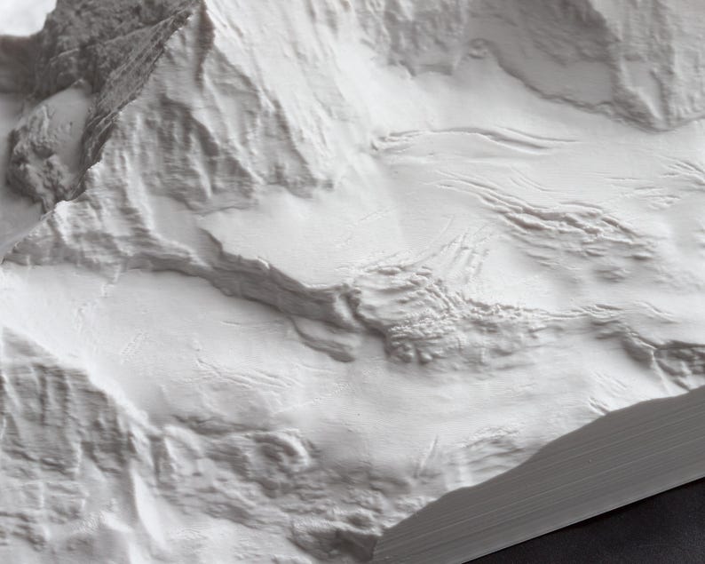 Puede incluir: Primer plano de un modelo de cordillera de monta&ntilde;as impreso en 3D blanco y texturizado. El modelo est&aacute; detallado con crestas y valles, creando una representaci&oacute;n realista de un paisaje monta&ntilde;oso.