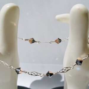 May include: A silver chain bracelet with rose gold accents and black crystal beads. The bracelet features a delicate, intricate design.
