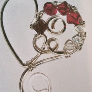 May include: A silver wire heart-shaped pendant with red and clear crystals.
