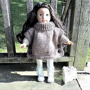 May include: A doll with long dark hair wearing a brown knit poncho sweater with black buttons and white boots. The doll is posed on a wooden bench outdoors.