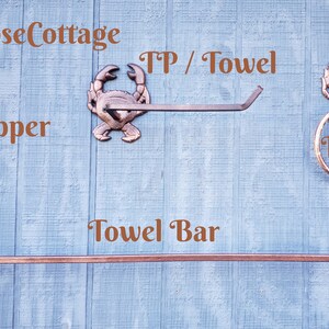 May include: Copper-colored crab-themed bathroom hardware set. Includes a towel bar, toilet paper holder, and towel ring. The items are mounted on a light blue wooden background. The text "CozyRoseCottage" and "Copper" are visible.