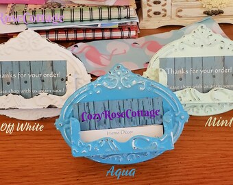 May include: Three ornate, oval-shaped, decorative holders in creamy off-white, aqua, and mint green. Each holder has a distressed finish and a slot for a card. The aqua holder is in the center. The text "Thanks for your order!" is visible on the cards.