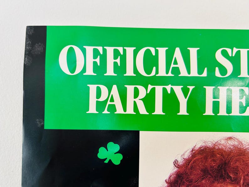May include: A poster with the words "OFFICIAL ST. PARTY HEADQUARTERS" in white letters on a green background. A green shamrock is in the lower left corner. The background is black.