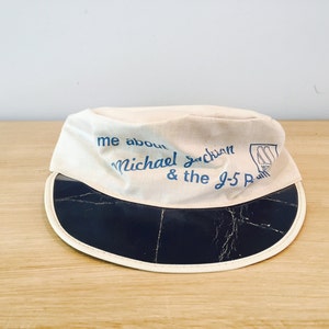 May include: A white canvas hat with a black brim and blue text that reads "me about Michael Jackson & the J-5 Paul".