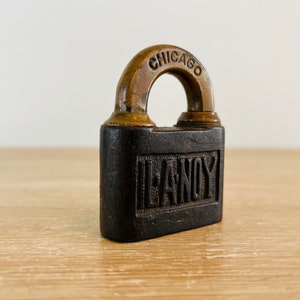 May include: A vintage black padlock with a brass arch and the words "CHICAGO" and "LEANOY" embossed on it.