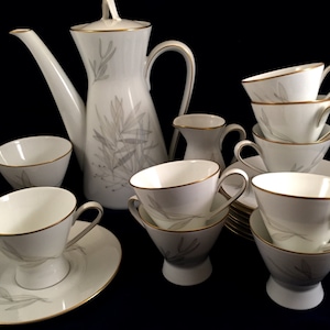 May include: A white porcelain tea set with a silver leaf design and gold trim. The set includes a teapot, creamer, sugar bowl, and six cups and saucers.