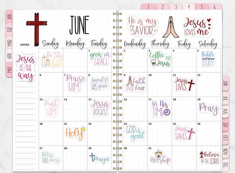 Puede incluir: Una agenda espiral abierta en junio, con una cruz roja y varias pegatinas con frases religiosas como "Jes&uacute;s es el camino" y "Ora". El calendario tiene un dise&ntilde;o de cuadr&iacute;cula con entradas diarias.