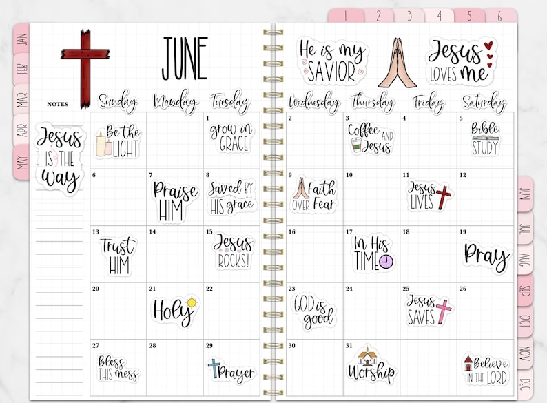 Puede incluir: Un planificador de espiral abierto en junio, con un dise&ntilde;o de cuadr&iacute;cula y pegatinas religiosas. Las pegatinas presentan frases y s&iacute;mbolos como cruces y manos en oraci&oacute;n. El planificador tiene pesta&ntilde;as rosas.