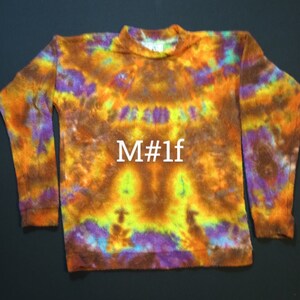 May include: A long-sleeved, tie-dye sweater in shades of orange, yellow, purple, and brown. The sweater has a crew neck and a fuzzy texture. The text "M#1f" is printed in white on the front of the sweater.