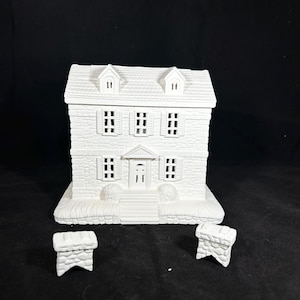 May include: A white ceramic house figurine featuring a textured stone-like exterior, a gabled roof with two dormer windows, and a central front door. The structure includes two separate, matching stone-textured chimney pieces placed in front of the house.