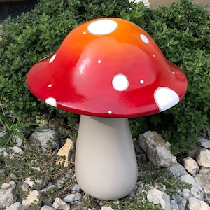 May include: A large red and orange mushroom garden statue with white polka dots. The mushroom has a white stem and is sitting on a bed of small gray rocks.