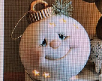 May include: A white ceramic ornament shaped like a smiling face with a winking eye. The ornament has a gold loop at the top and a black and white striped band around the middle.