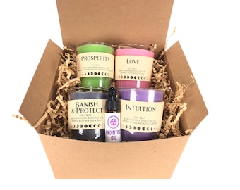 May include: A brown cardboard box filled with shredded paper contains four soy wax candles and a small bottle of anointing oil. The candles are labeled "Prosperity", "Love", "Banish & Protect", and "Intuition".